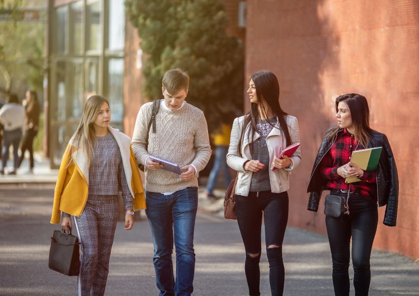 Four university students talk and walk across a Denton university campus with their bookbags in hand.